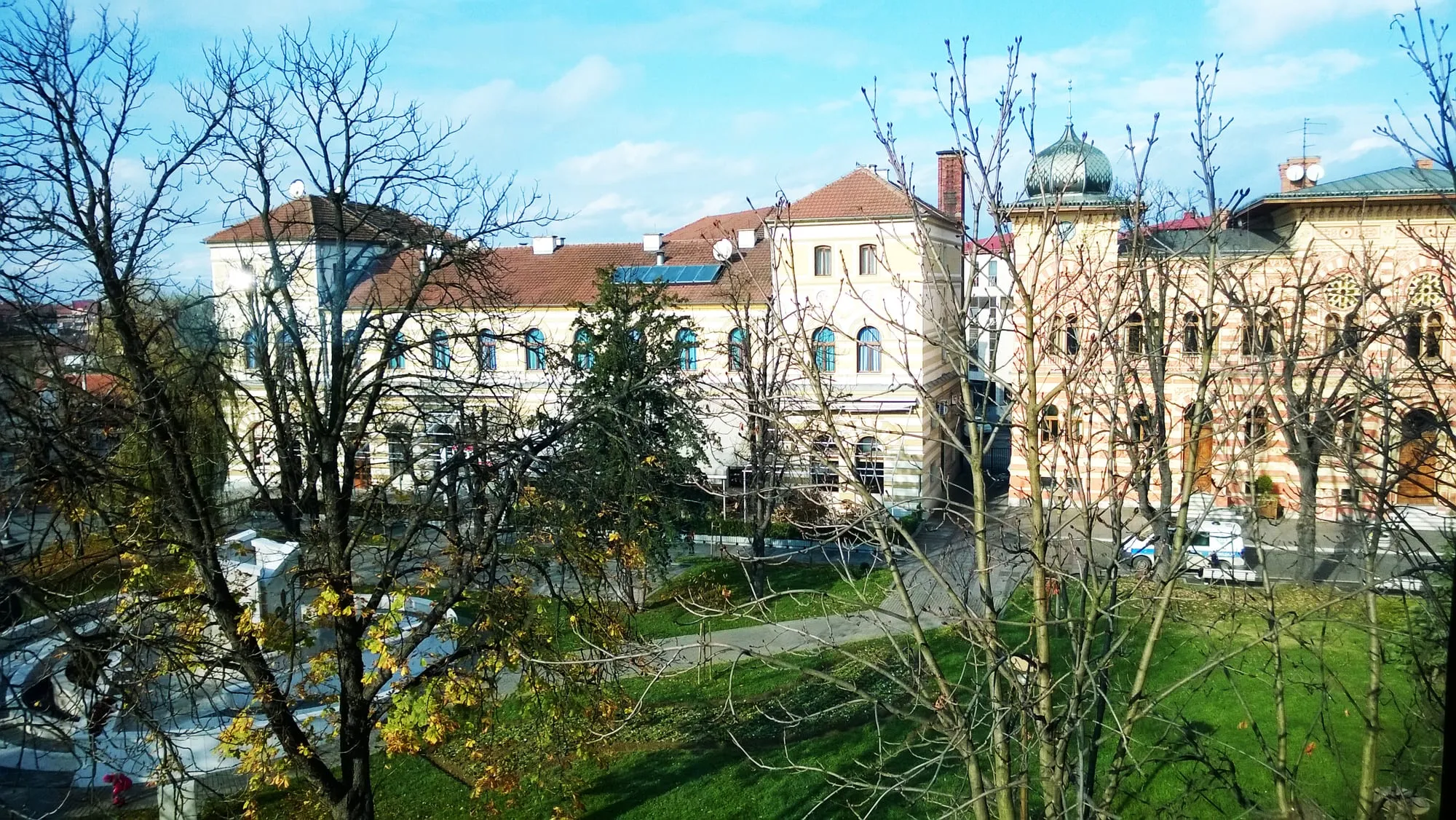 Zgrada Vijećnice sa kupolom i hotel Posavina u Brčkom, ispred je park sa jesenjim drvećem.