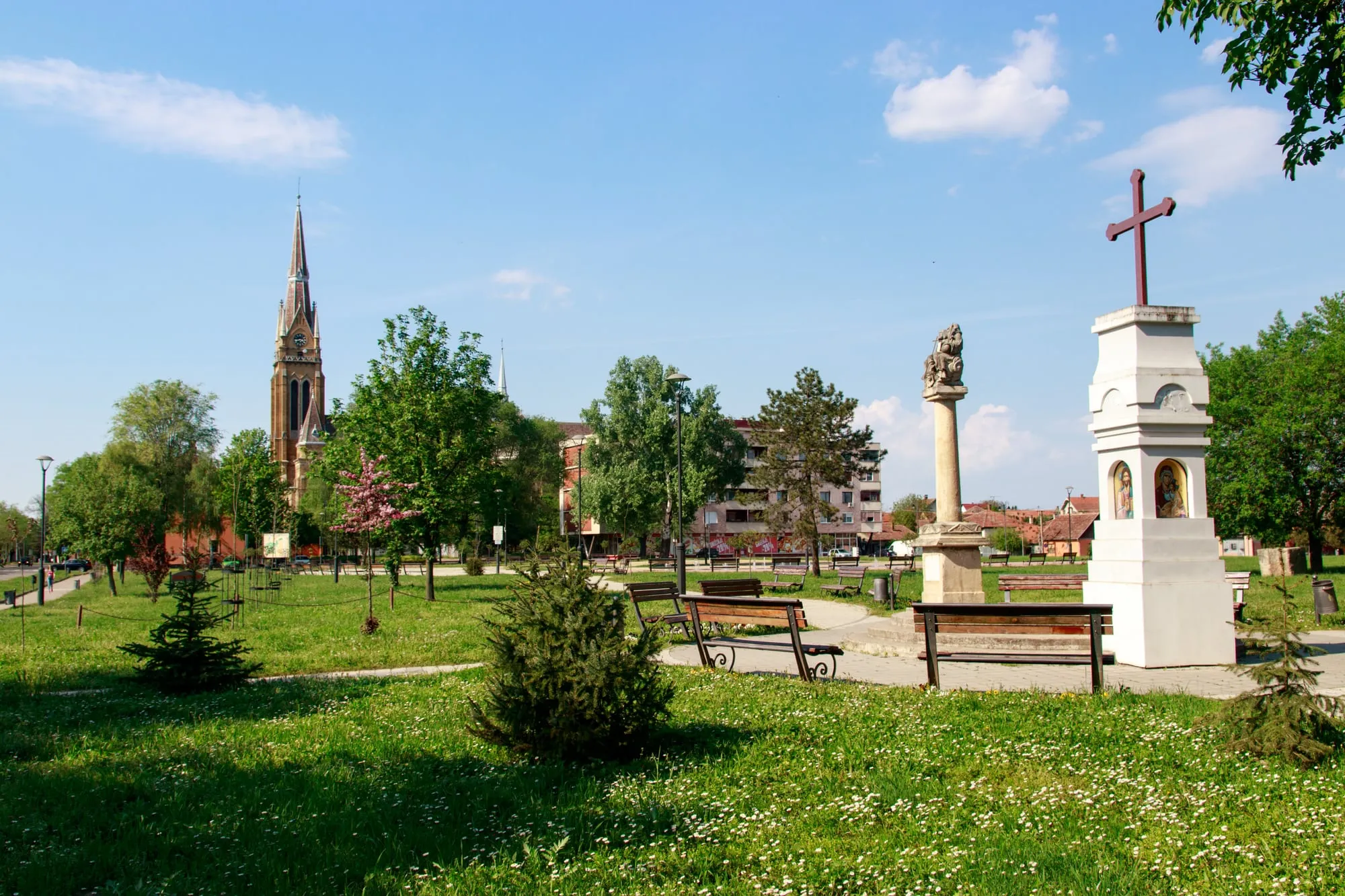 Glavni trg u Bačkoj Topoli: park sa klupama, u pozadini toranj crkve, desno spomenik na stubu i bela kapelica sa krstom.