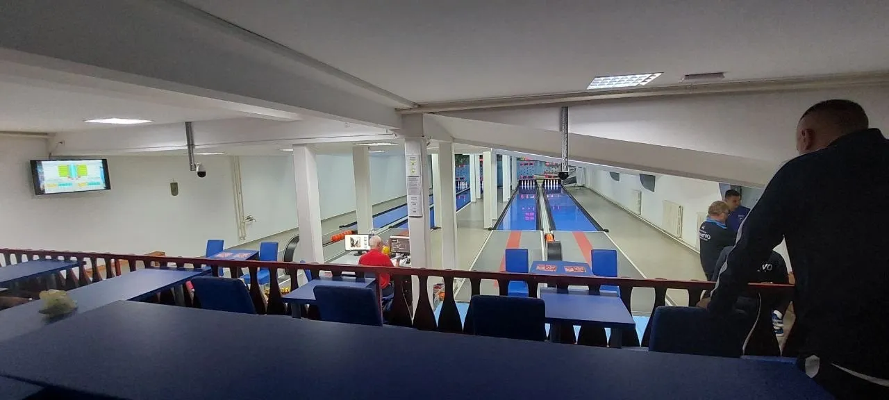 Galerija sa stolovima i stolicama iznad staza, na zidu ekran sa rezultatima.