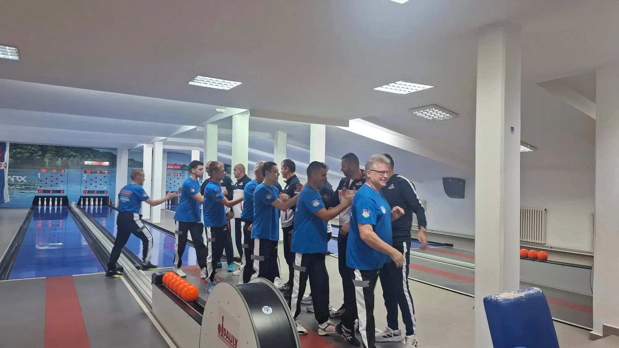Igrači u plavim majicama i igrači u teget-belim trenerkama rukuju se u prolazu između staza.