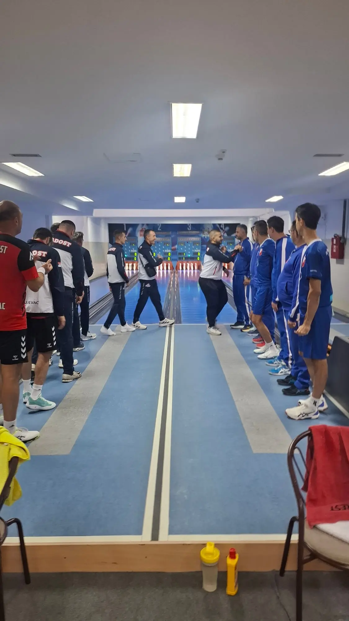 Igrači Mladosti u teget-belim trenerkama prolaze između staza i pozdravljaju se sa igračima Vojvodine u plavom.