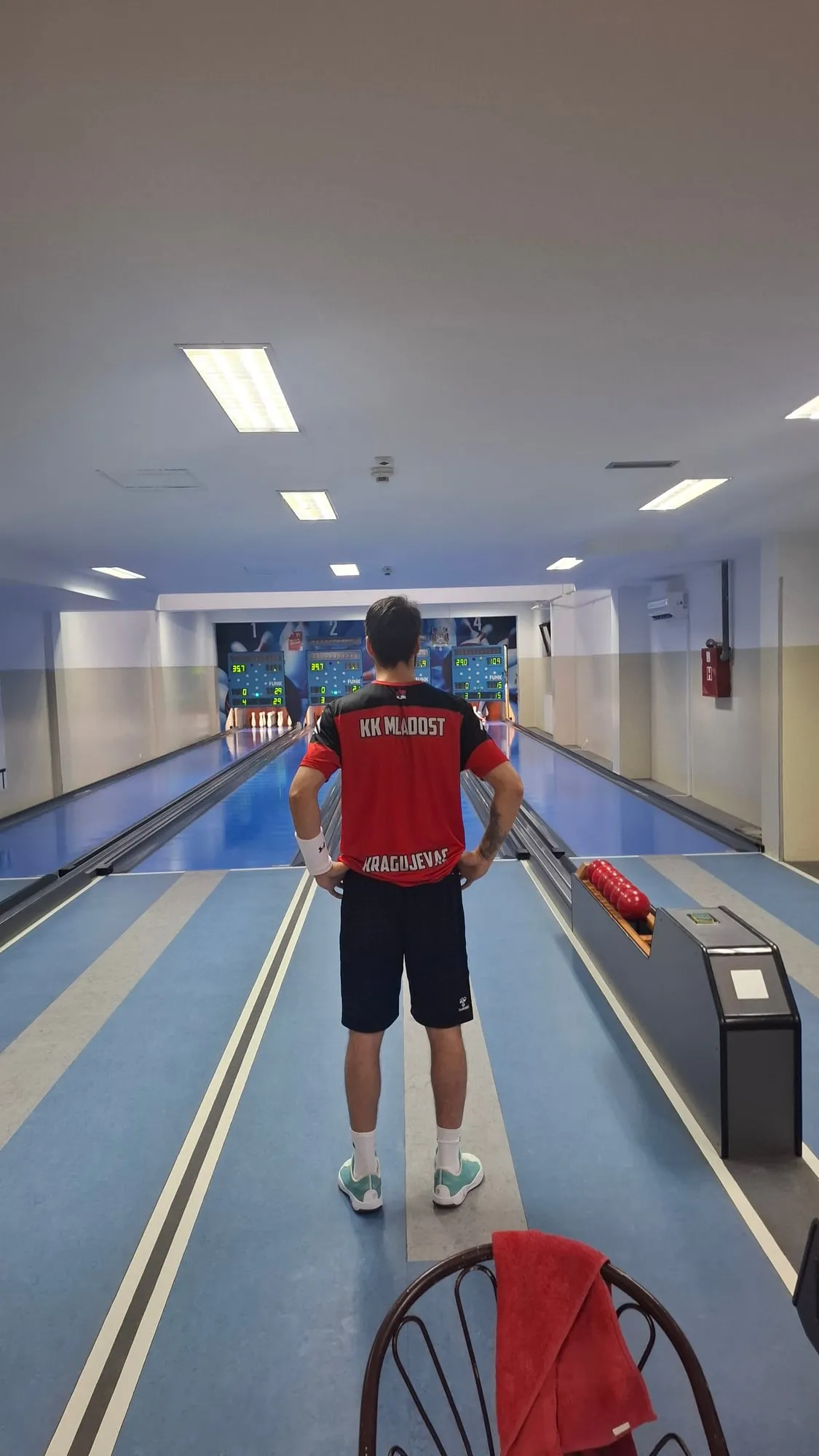 Igrač u crveno-crnoj majici sa natpisom KK Mladost Kragujevac stoji okrenut leđima, sa rukama na bokovima, ispred staze i semafora.