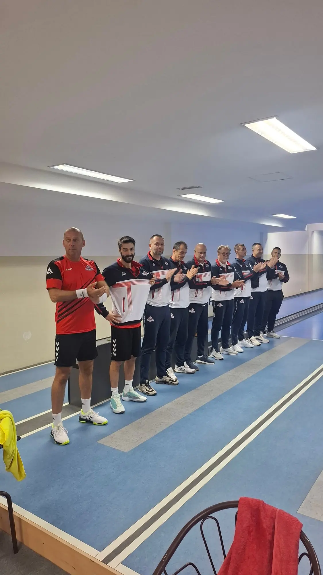 Igrači Mladosti postrojeni u vrsti između staza aplaudiraju; prvi je u crveno-crnoj majici, ostali u teget-belim trenerkama.