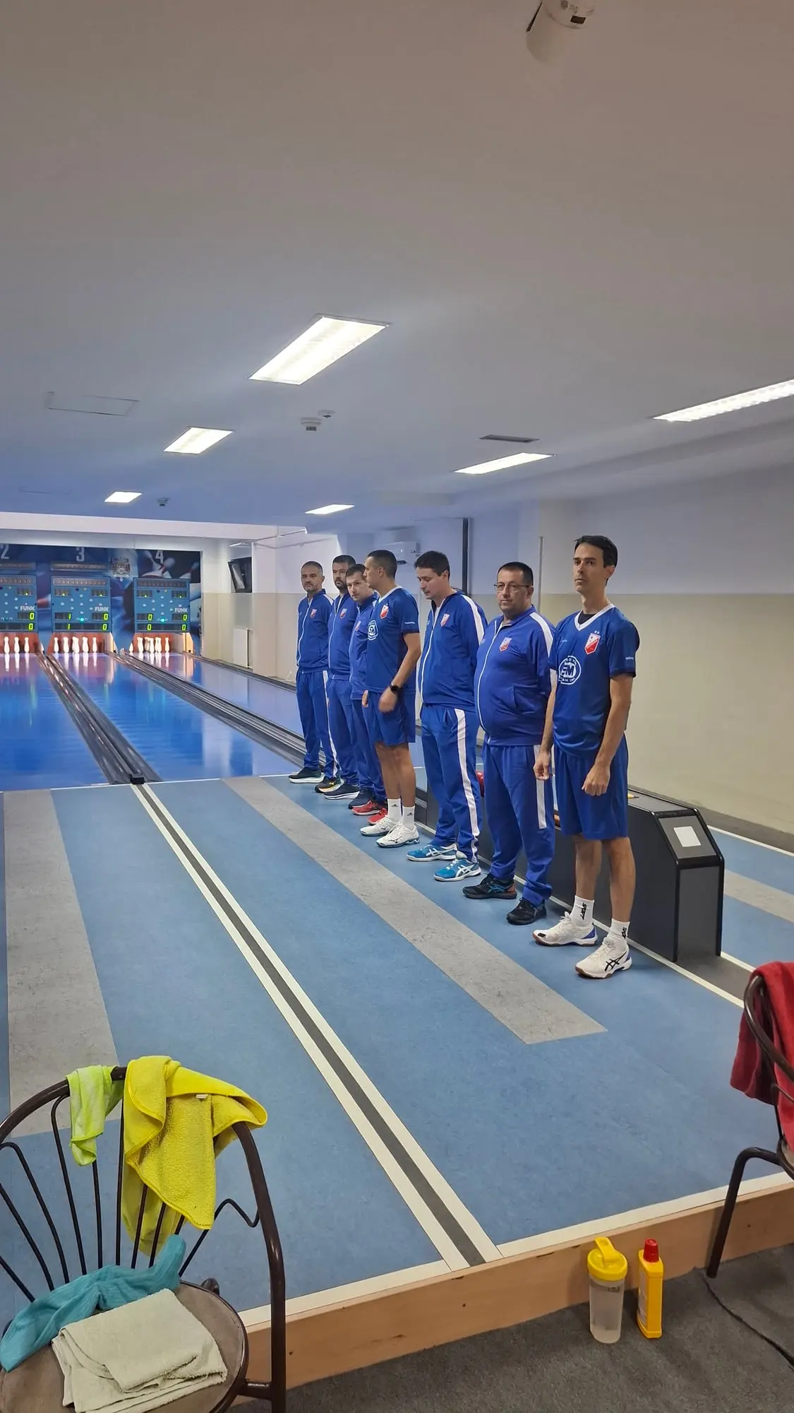 Igrači Vojvodine u plavim trenerkama i majicama postrojeni u vrsti između staza; iza su semafori sa nulama.