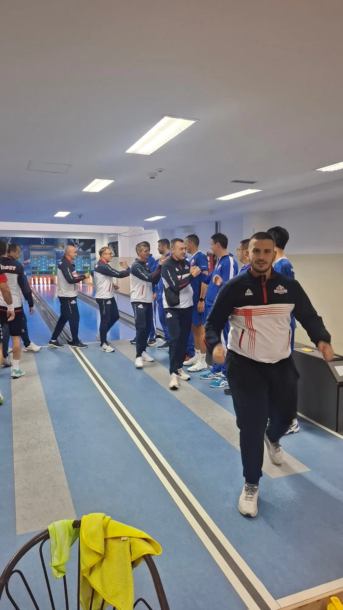 Igrač u teget-beloj trenerci Mladosti ide ka kameri; iza se igrači Mladosti i Vojvodine rukuju između staza.